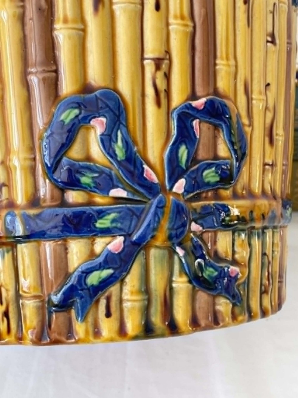 A cylindrical Victorian majolica jardiniere decorated with a moulded bamboo cane pattern in yellow and brown tones, wrapped with a blue ribbon tied in a bow. View VIII