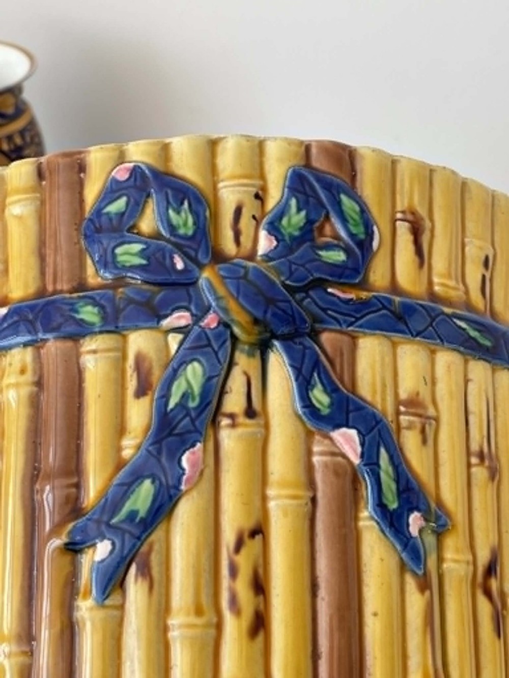 A cylindrical Victorian majolica jardiniere decorated with a moulded bamboo cane pattern in yellow and brown tones, wrapped with a blue ribbon tied in a bow. View IX