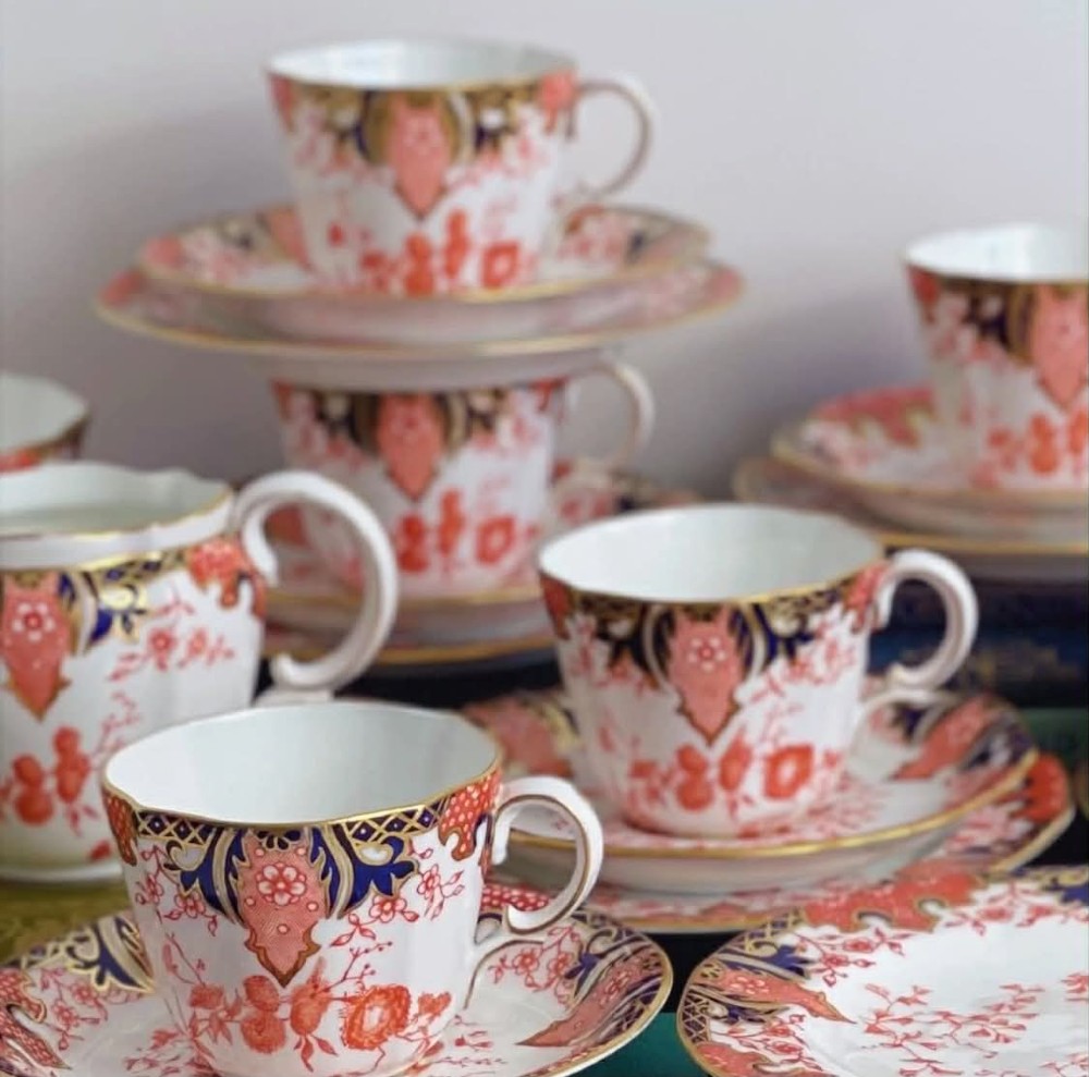 An antique Royal Crown Derby bone china tea set featuring iron red and cobalt blue foliage motifs with gold gilding across cups, saucers, and a cream pitcher.
