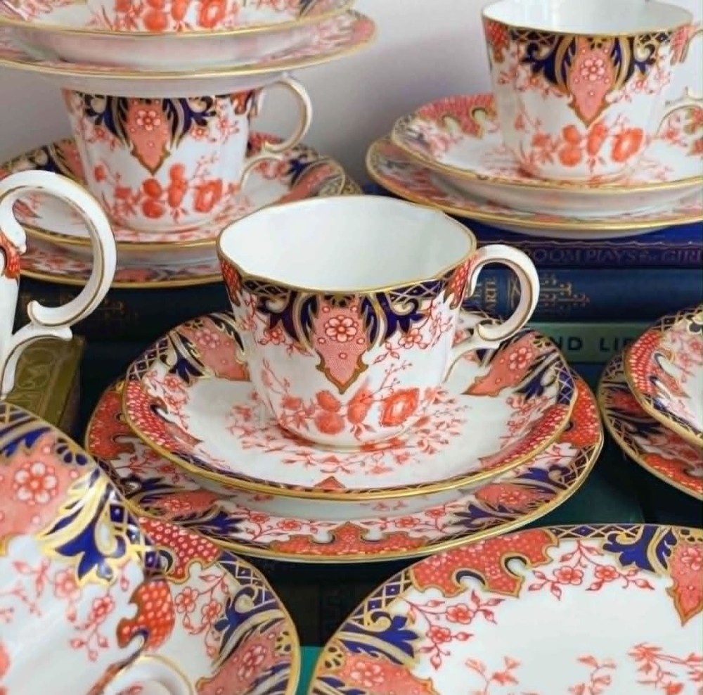 An antique Royal Crown Derby bone china tea set featuring iron red and cobalt blue foliage motifs with gold gilding across cups, saucers, and a cream pitcher. View II