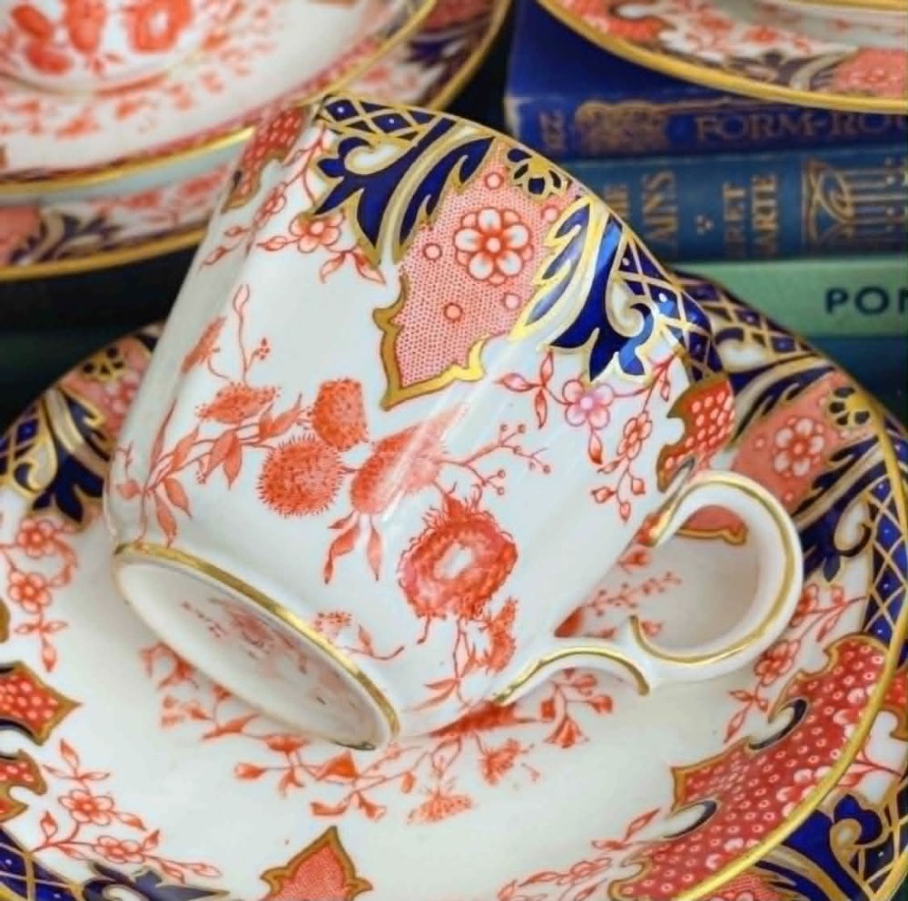 An antique Royal Crown Derby bone china tea set featuring iron red and cobalt blue foliage motifs with gold gilding across cups, saucers, and a cream pitcher. View III
