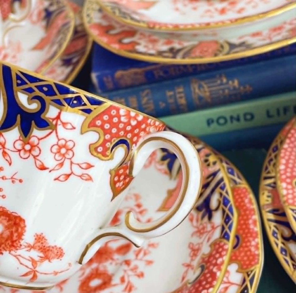 An antique Royal Crown Derby bone china tea set featuring iron red and cobalt blue foliage motifs with gold gilding across cups, saucers, and a cream pitcher. View IV