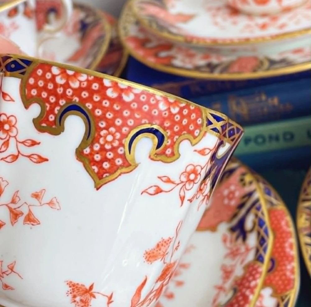An antique Royal Crown Derby bone china tea set featuring iron red and cobalt blue foliage motifs with gold gilding across cups, saucers, and a cream pitcher. View V