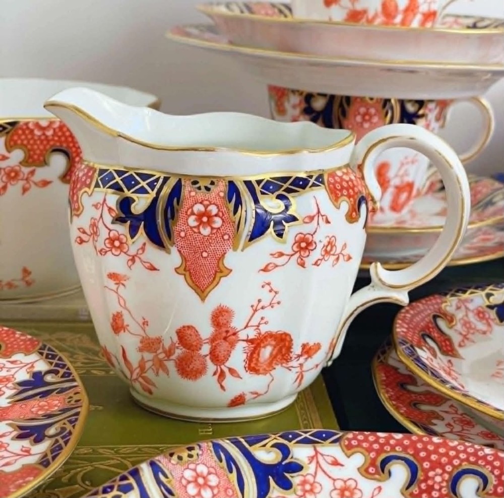 An antique Royal Crown Derby bone china tea set featuring iron red and cobalt blue foliage motifs with gold gilding across cups, saucers, and a cream pitcher. View IX