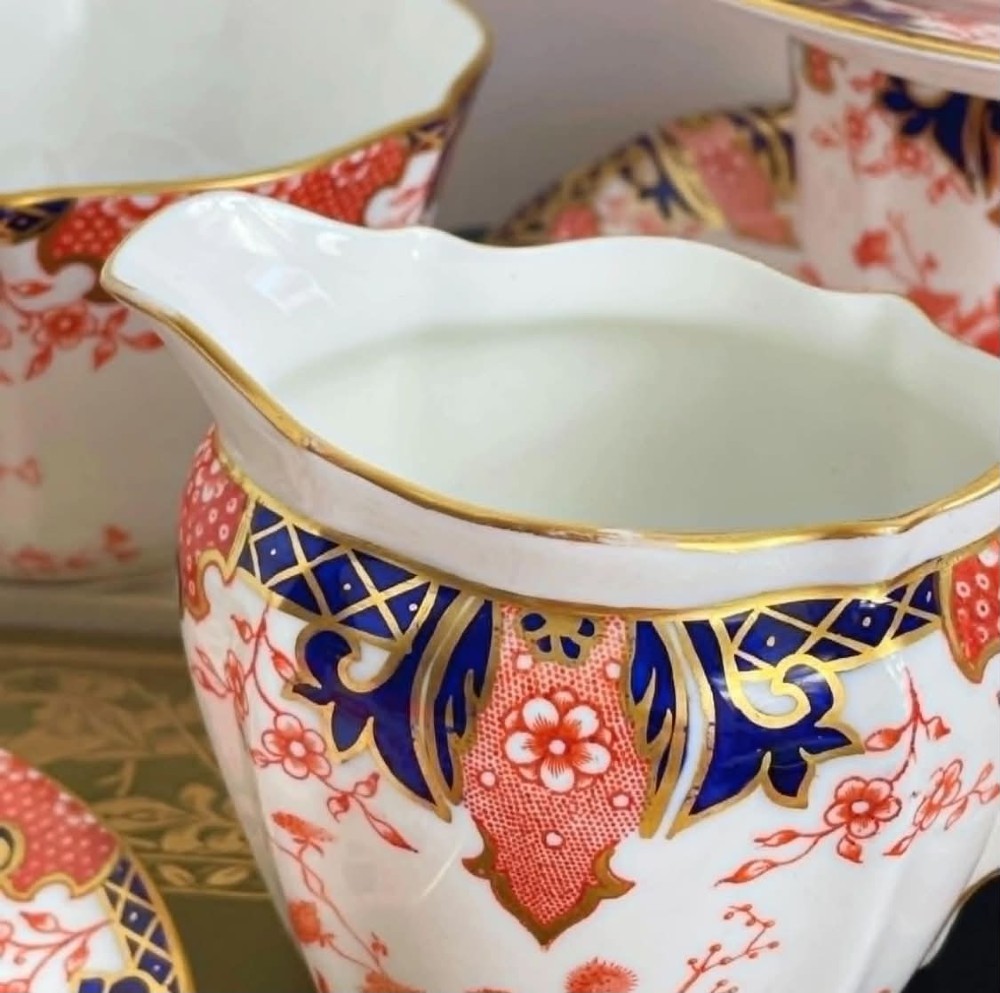 An antique Royal Crown Derby bone china tea set featuring iron red and cobalt blue foliage motifs with gold gilding across cups, saucers, and a cream pitcher. View X