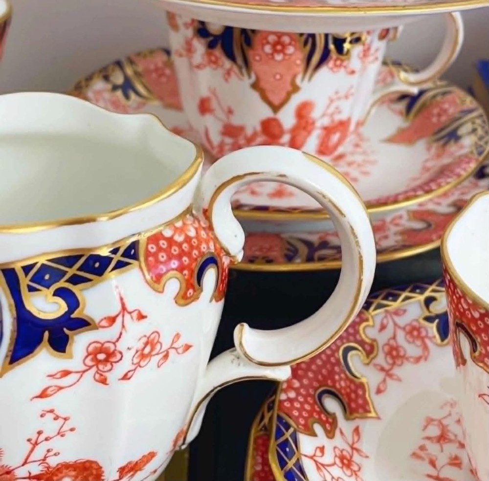 An antique Royal Crown Derby bone china tea set featuring iron red and cobalt blue foliage motifs with gold gilding across cups, saucers, and a cream pitcher. View XI