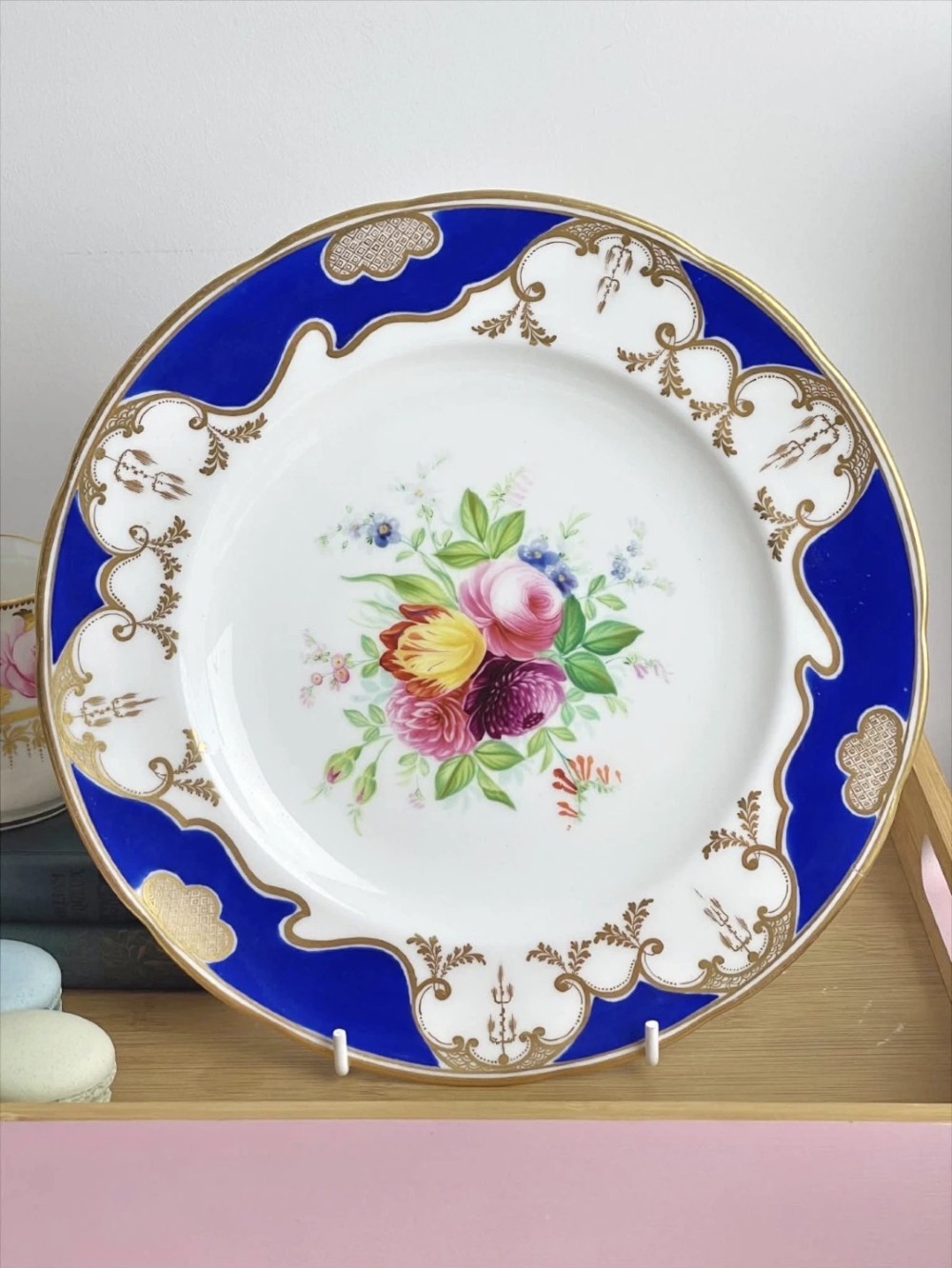 A circular porcelain dessert plate featuring a central hand-painted floral bouquet surrounded by a cobalt blue rim with gilded scrollwork.