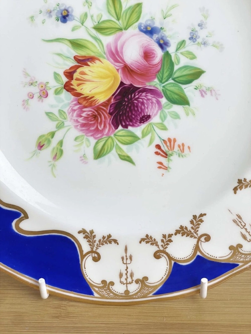 A circular porcelain dessert plate featuring a central hand-painted floral bouquet surrounded by a cobalt blue rim with gilded scrollwork. View II