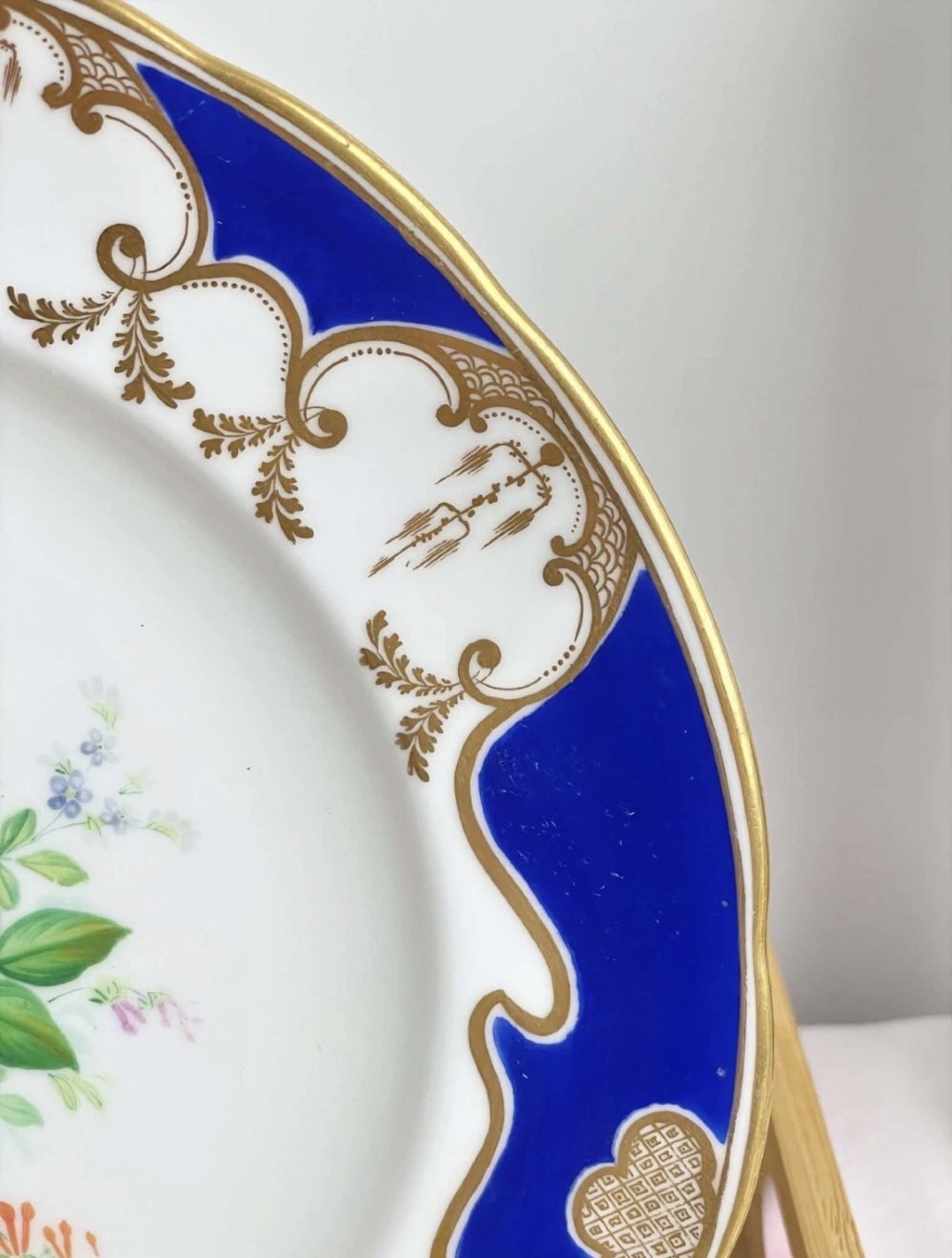 A circular porcelain dessert plate featuring a central hand-painted floral bouquet surrounded by a cobalt blue rim with gilded scrollwork. View IV