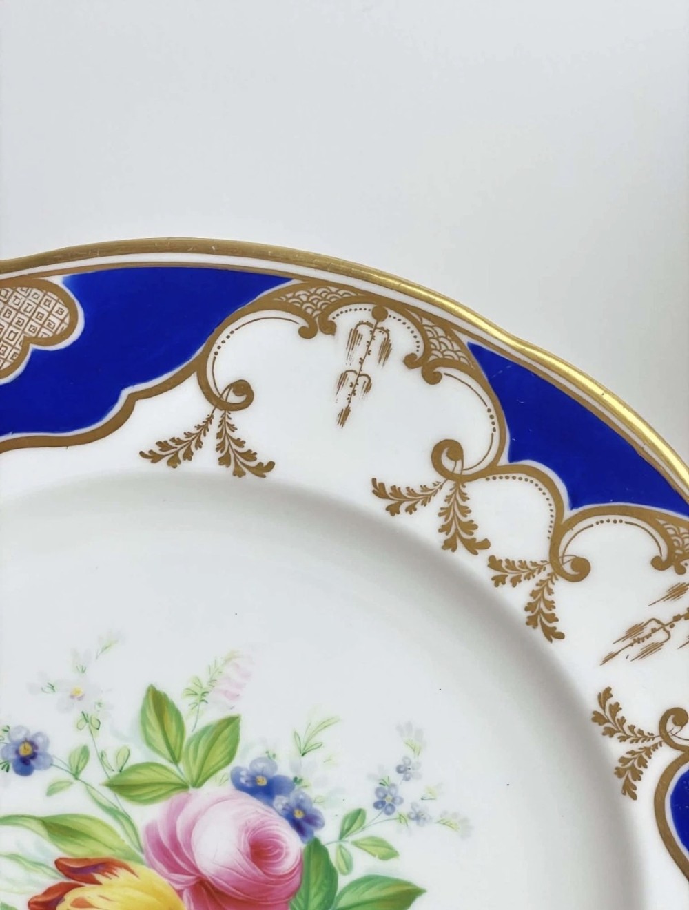 A circular porcelain dessert plate featuring a central hand-painted floral bouquet surrounded by a cobalt blue rim with gilded scrollwork. View V