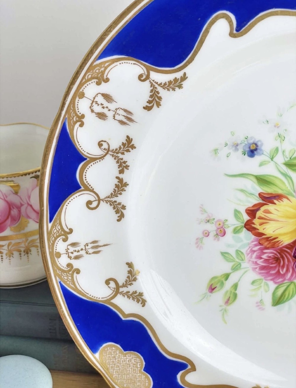 A circular porcelain dessert plate featuring a central hand-painted floral bouquet surrounded by a cobalt blue rim with gilded scrollwork. View VII