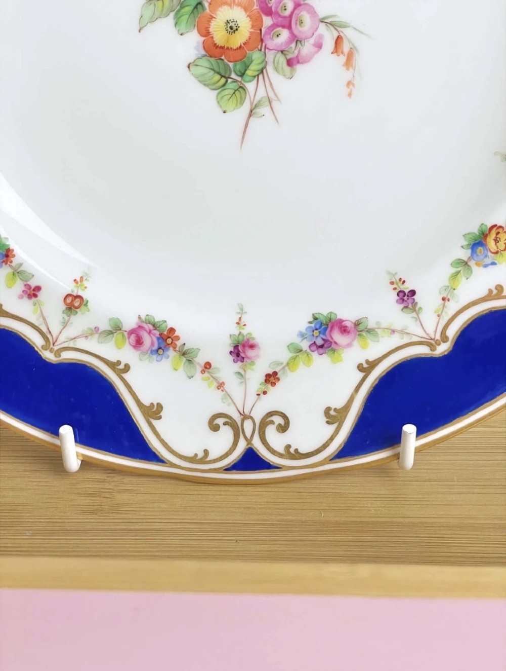 An antique circular porcelain dessert plate featuring a hand-painted central floral spray, delicate floral swags, and a scalloped cobalt blue and gilded rim. View II