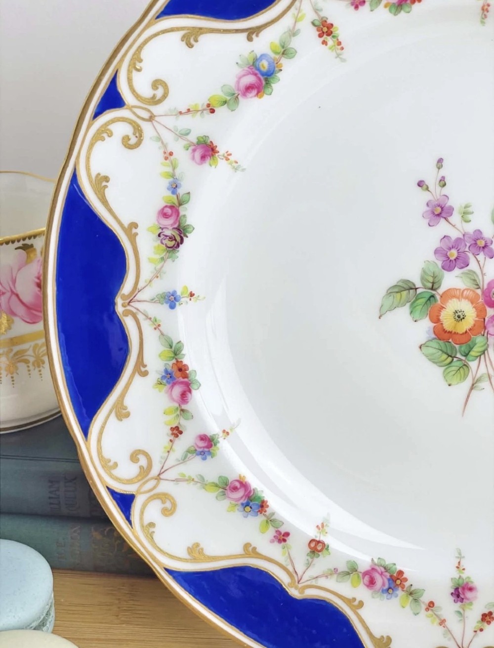 An antique circular porcelain dessert plate featuring a hand-painted central floral spray, delicate floral swags, and a scalloped cobalt blue and gilded rim. View VII