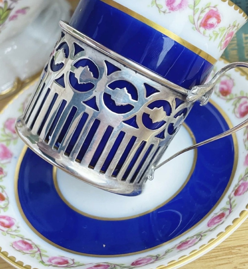 A cobalt blue porcelain coffee can decorated with pink floral swags, set inside a pierced sterling silver holder with a matching saucer. View III