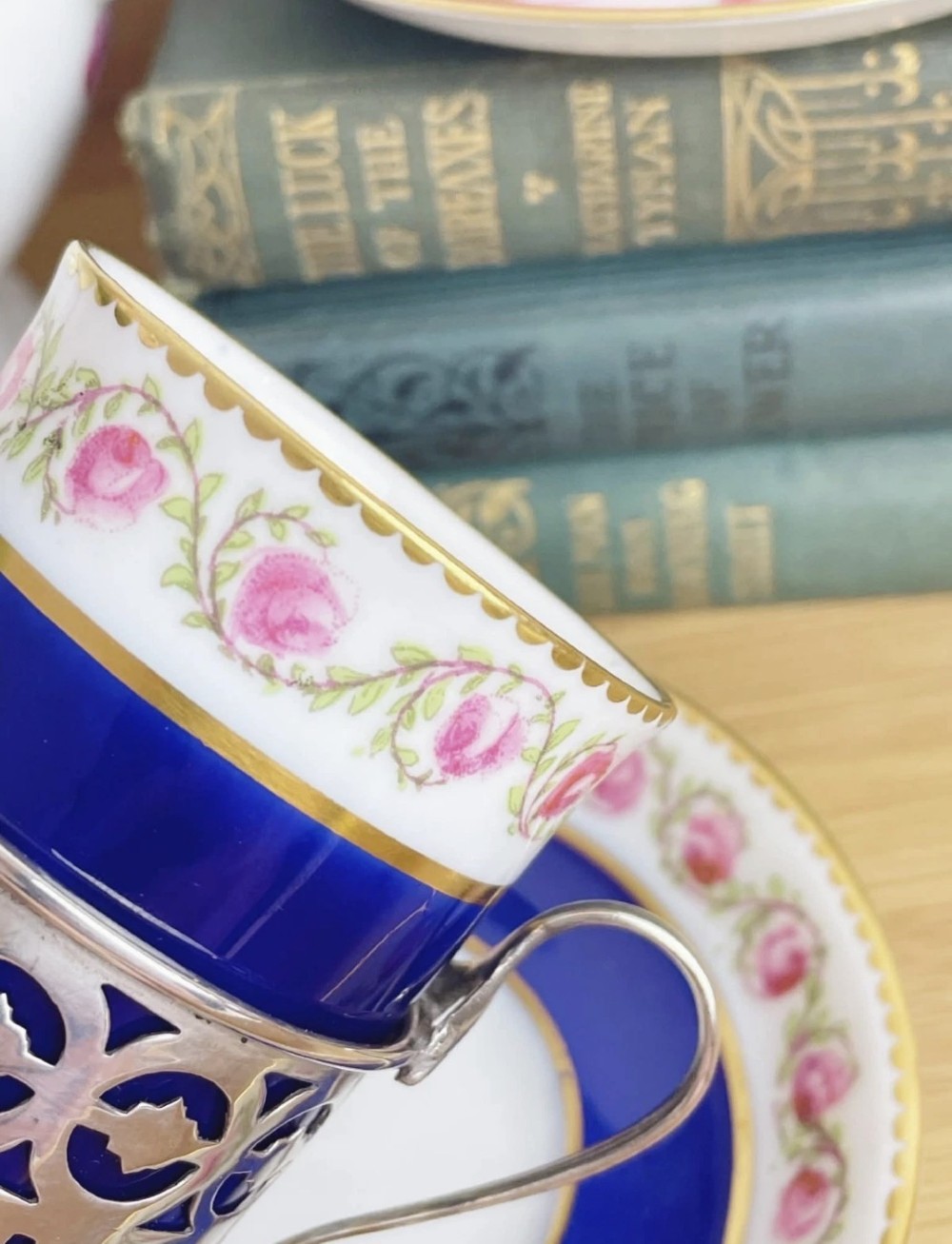 A cobalt blue porcelain coffee can decorated with pink floral swags, set inside a pierced sterling silver holder with a matching saucer. View VI