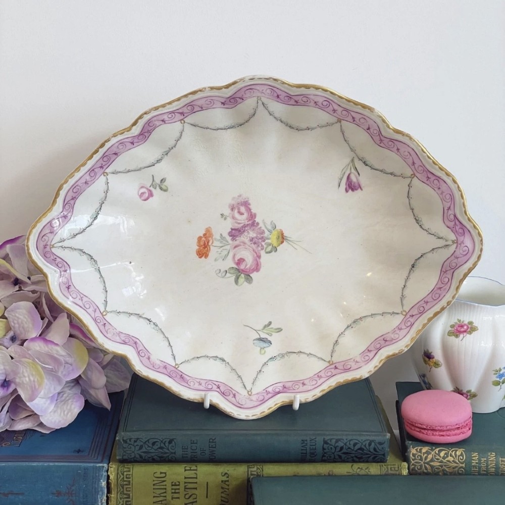 An eighteenth-century oval Derby porcelain serving dish with a scalloped rim, pink scroll border with gilt detailing, and central hand-painted floral spray.