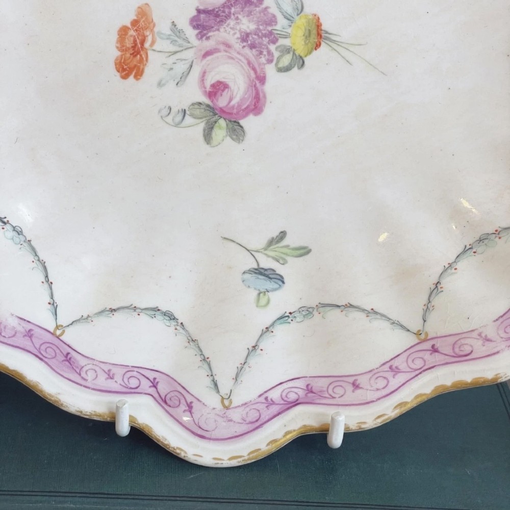 An eighteenth-century oval Derby porcelain serving dish with a scalloped rim, pink scroll border with gilt detailing, and central hand-painted floral spray. View II