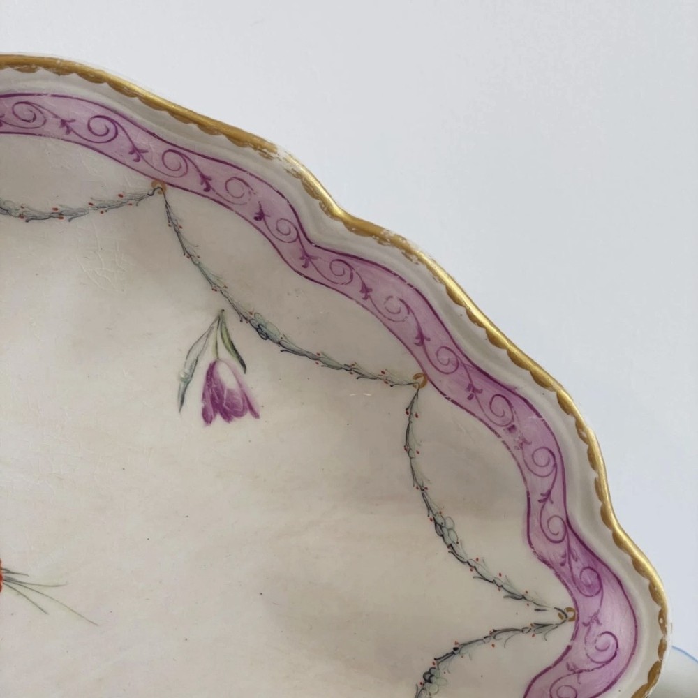 An eighteenth-century oval Derby porcelain serving dish with a scalloped rim, pink scroll border with gilt detailing, and central hand-painted floral spray. View V