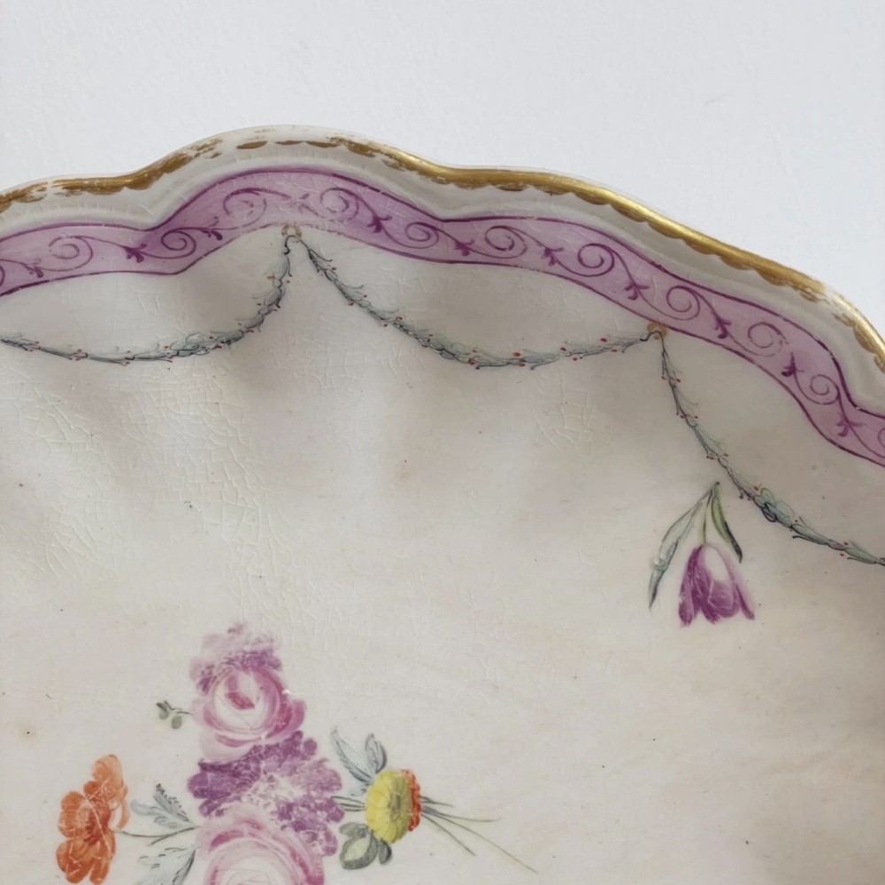 An eighteenth-century oval Derby porcelain serving dish with a scalloped rim, pink scroll border with gilt detailing, and central hand-painted floral spray. View VI