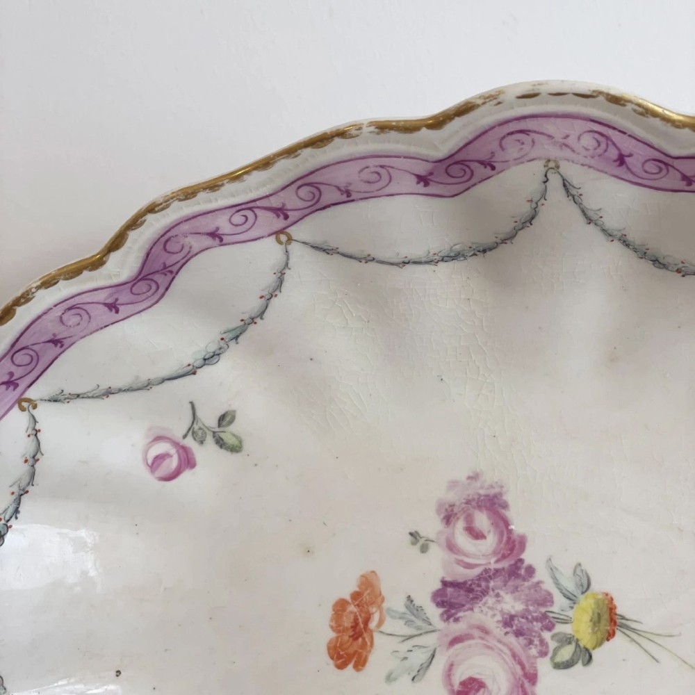 An eighteenth-century oval Derby porcelain serving dish with a scalloped rim, pink scroll border with gilt detailing, and central hand-painted floral spray. View VII