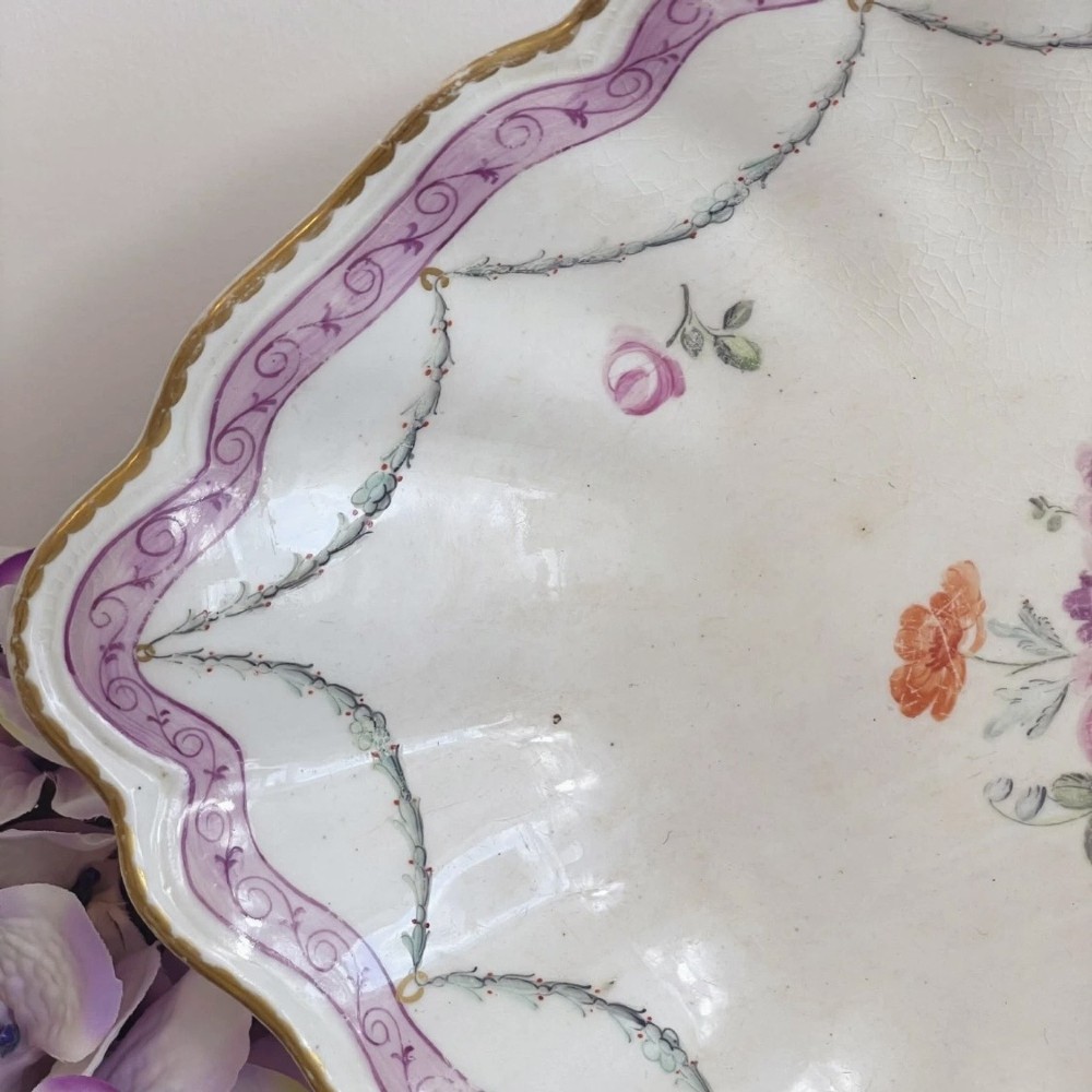 An eighteenth-century oval Derby porcelain serving dish with a scalloped rim, pink scroll border with gilt detailing, and central hand-painted floral spray. View XII