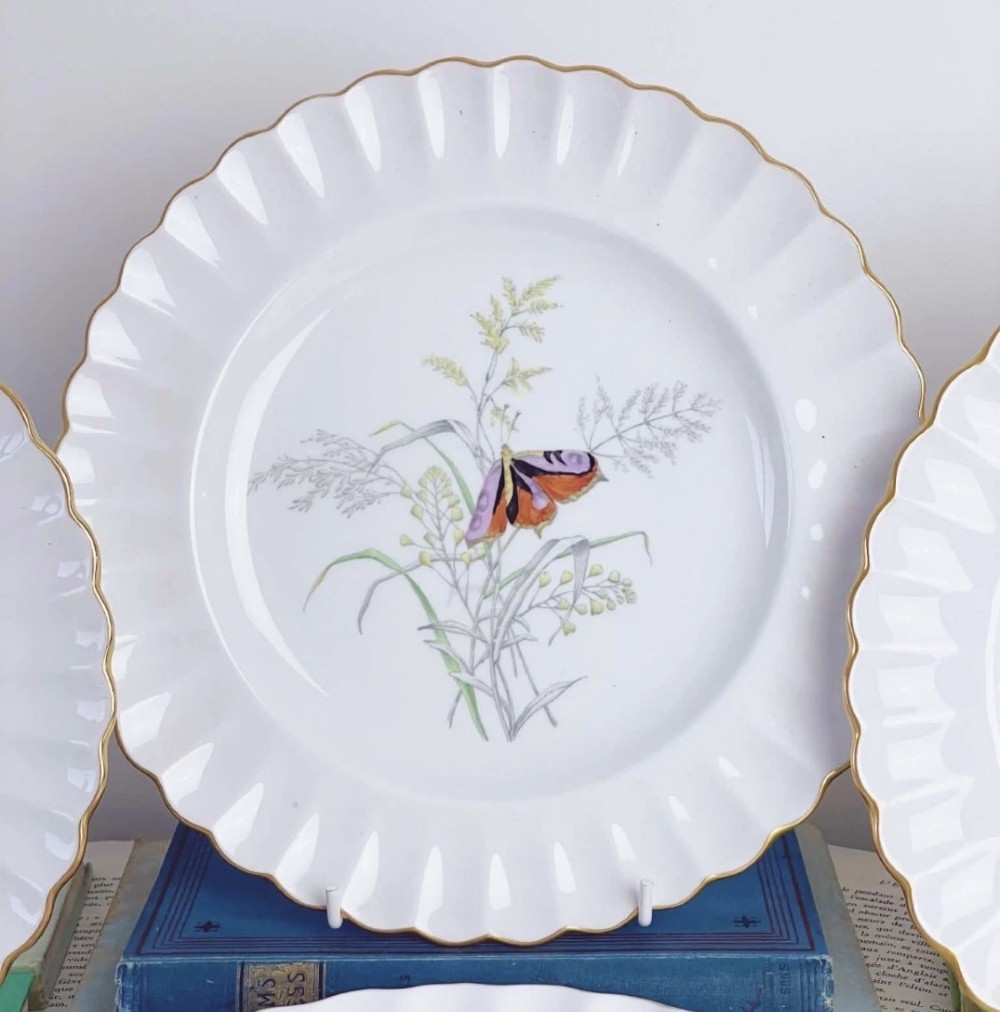 A set of white bone china dessert plates featuring scalloped gilded edges and botanical butterfly illustrations at the centre. View III