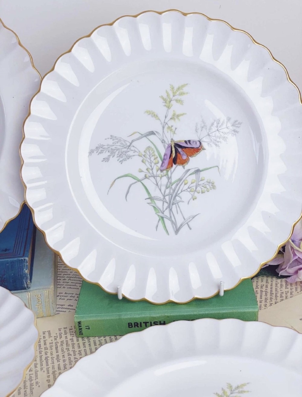 A set of white bone china dessert plates featuring scalloped gilded edges and botanical butterfly illustrations at the centre. View IV