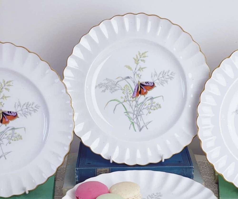 A set of white bone china dessert plates featuring scalloped gilded edges and botanical butterfly illustrations at the centre. View VII