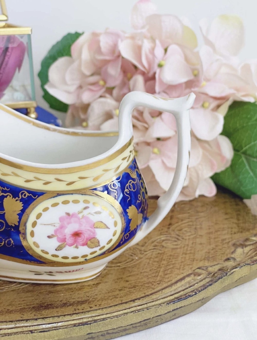 An antique Regency porcelain milk jug decorated with cobalt blue panels, gilt vine details, and hand-painted floral cartouches. View II