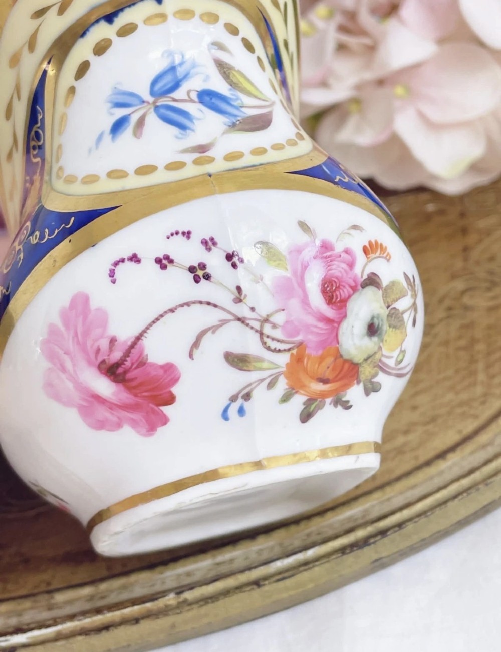 An antique Regency porcelain milk jug decorated with cobalt blue panels, gilt vine details, and hand-painted floral cartouches. View V