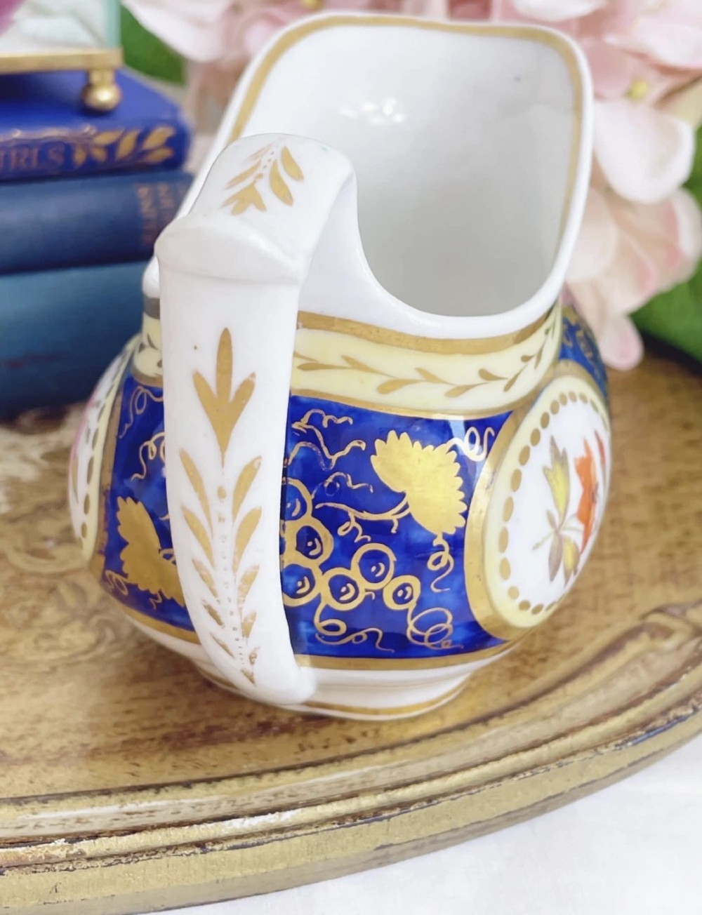 An antique Regency porcelain milk jug decorated with cobalt blue panels, gilt vine details, and hand-painted floral cartouches. View VIII