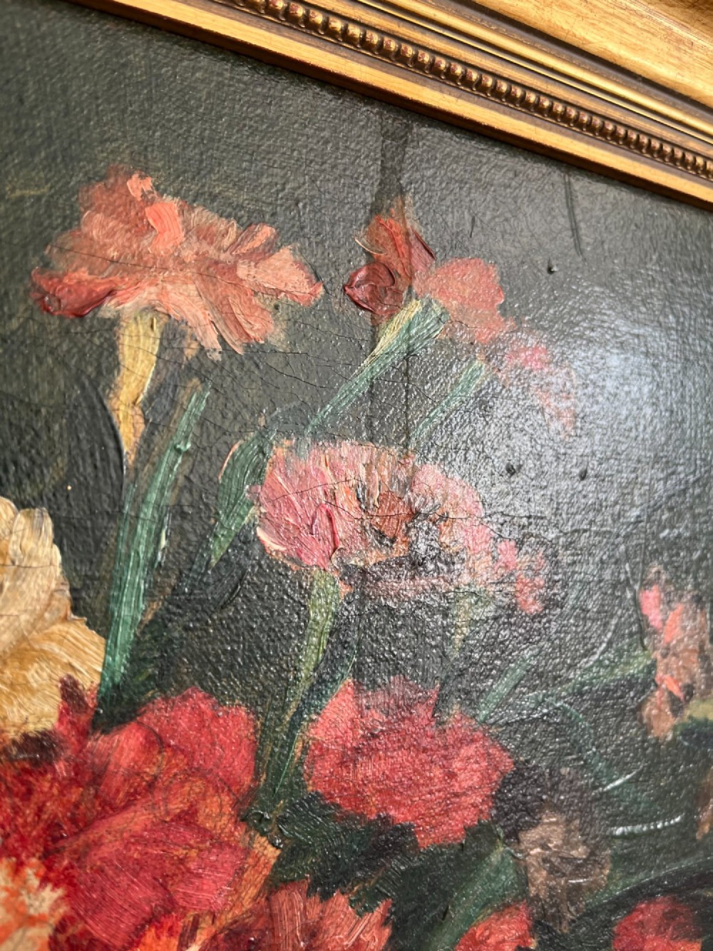 A horizontal oil painting depicting a bouquet of red, pink, yellow, and white carnations in a dark vase, enclosed within a moulded gilt frame. View II