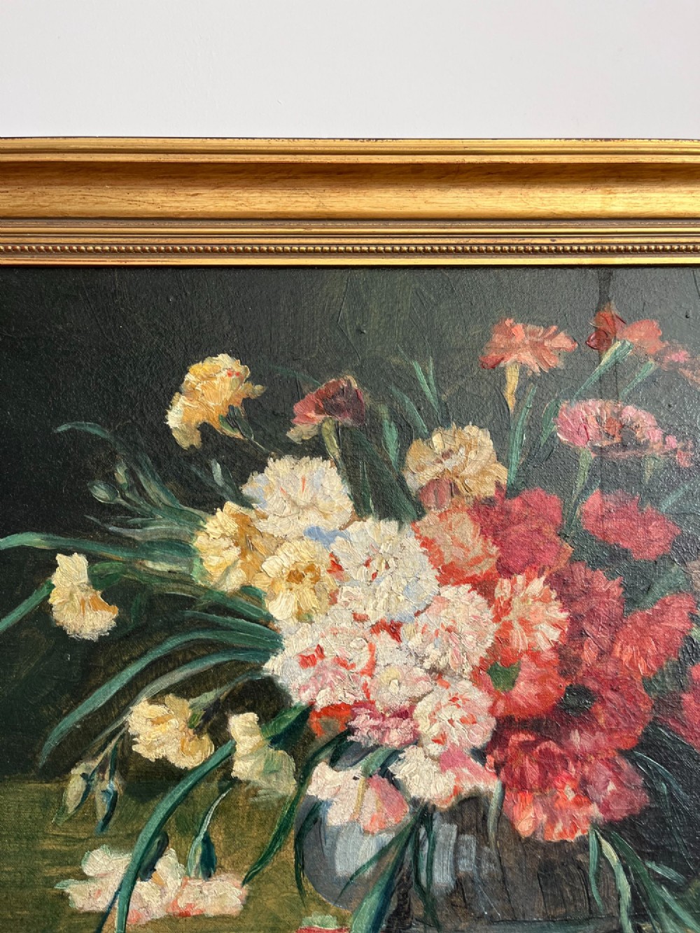 A horizontal oil painting depicting a bouquet of red, pink, yellow, and white carnations in a dark vase, enclosed within a moulded gilt frame. View X