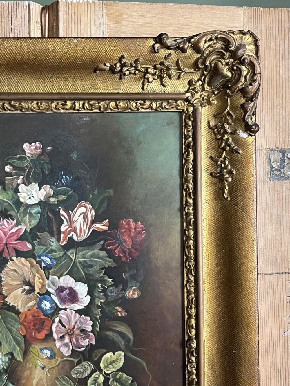 A framed oil painting depicting a floral arrangement in a urn with fruit at the base, housed within an ornate gilt gesso frame. View II