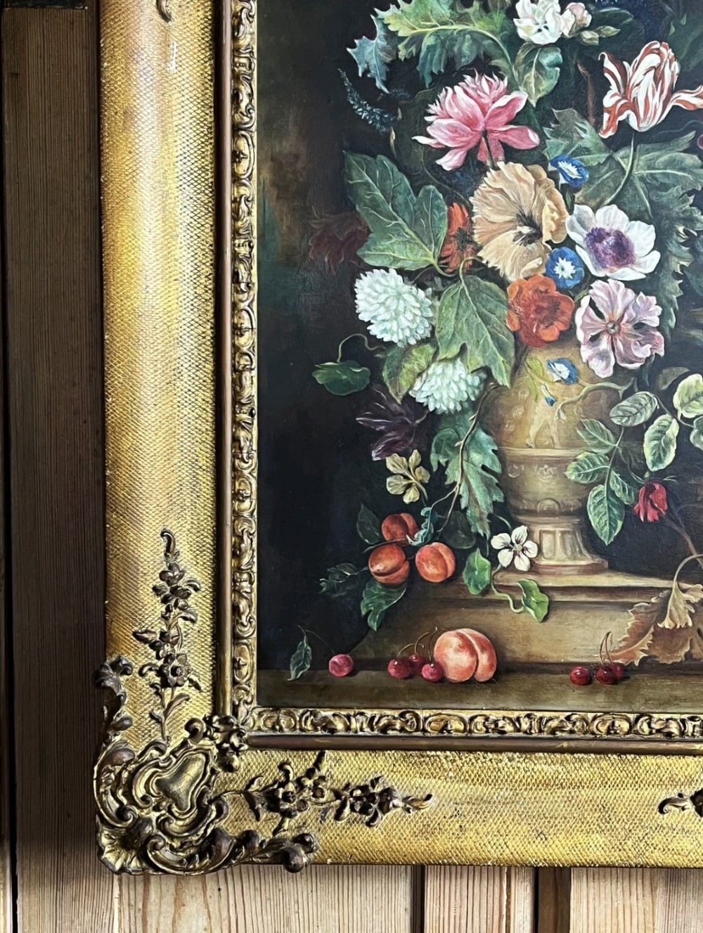A framed oil painting depicting a floral arrangement in a urn with fruit at the base, housed within an ornate gilt gesso frame. View V