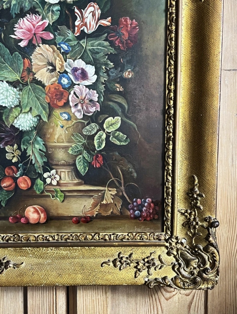 A framed oil painting depicting a floral arrangement in a urn with fruit at the base, housed within an ornate gilt gesso frame. View VI