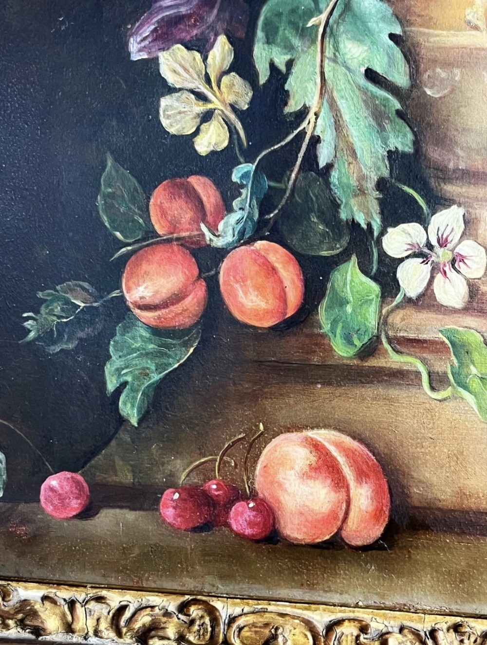 A framed oil painting depicting a floral arrangement in a urn with fruit at the base, housed within an ornate gilt gesso frame. View XI
