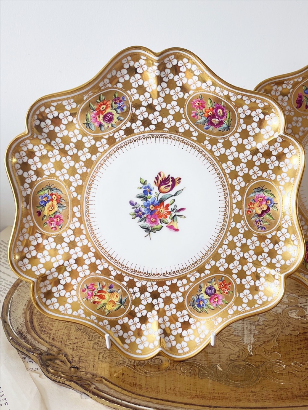 A pair of late Victorian Coalport bone china cabinet plates featuring scalloped rims heavily detailed with gold leaf, white geometric patterns, and central hand-painted floral sprays. View II