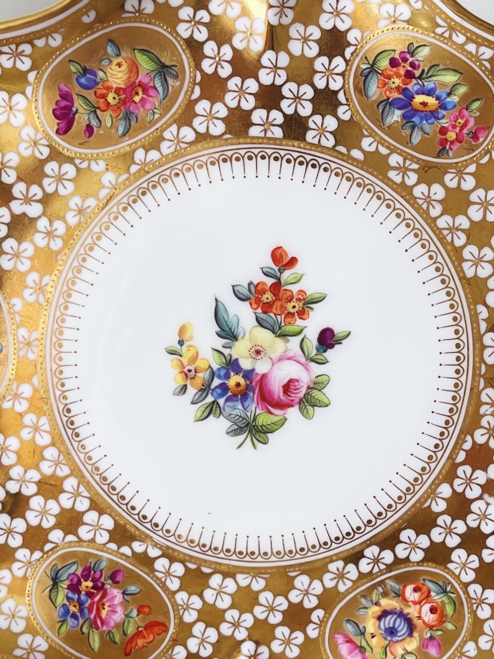 A pair of late Victorian Coalport bone china cabinet plates featuring scalloped rims heavily detailed with gold leaf, white geometric patterns, and central hand-painted floral sprays. View V