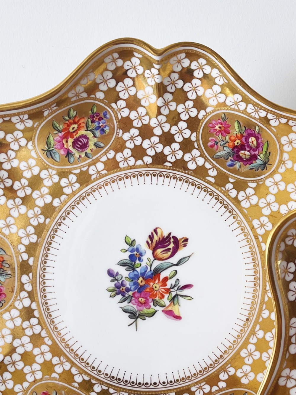 A pair of late Victorian Coalport bone china cabinet plates featuring scalloped rims heavily detailed with gold leaf, white geometric patterns, and central hand-painted floral sprays. View VII