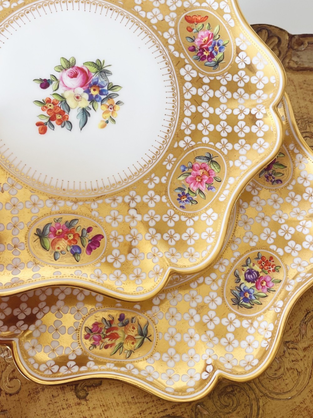 A pair of late Victorian Coalport bone china cabinet plates featuring scalloped rims heavily detailed with gold leaf, white geometric patterns, and central hand-painted floral sprays. View XIII