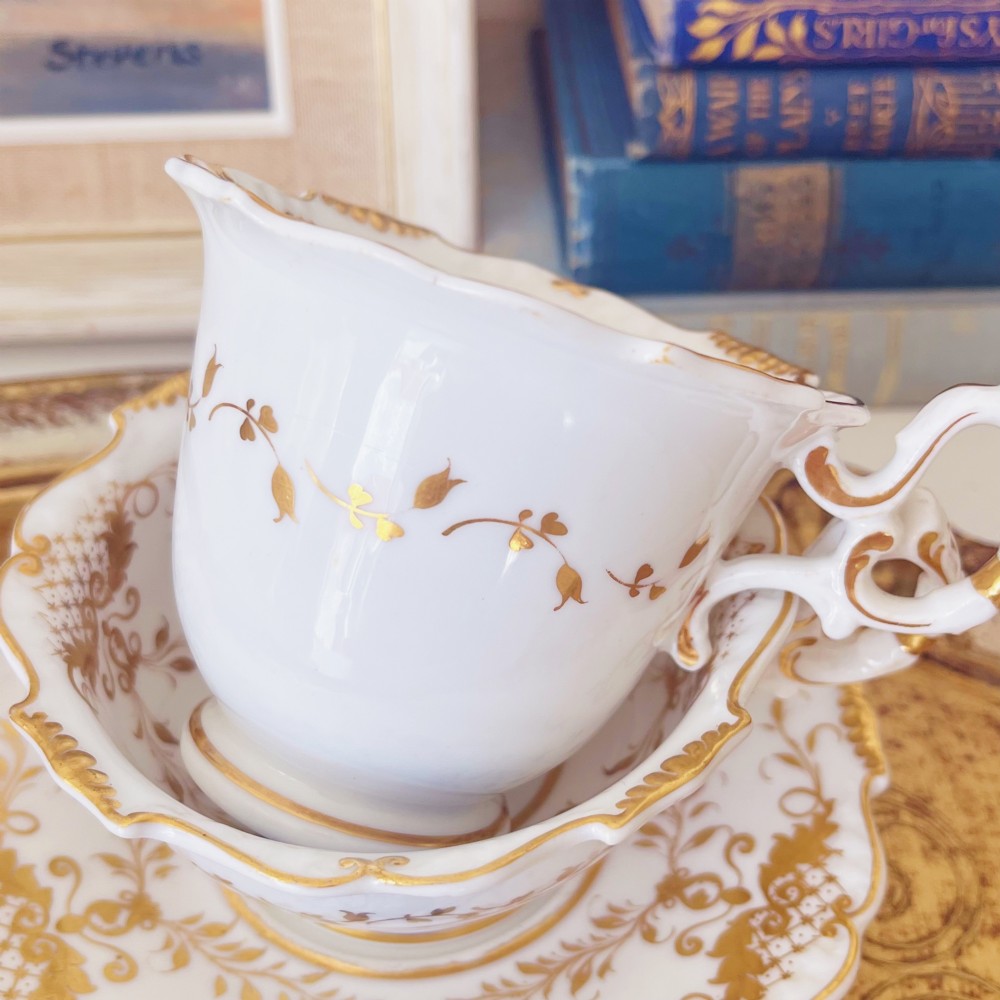 A Regency era porcelain tea trio comprising a teacup, coffee cup, and saucer decorated with blue floral hand-painting and gold leaf gilding. View II