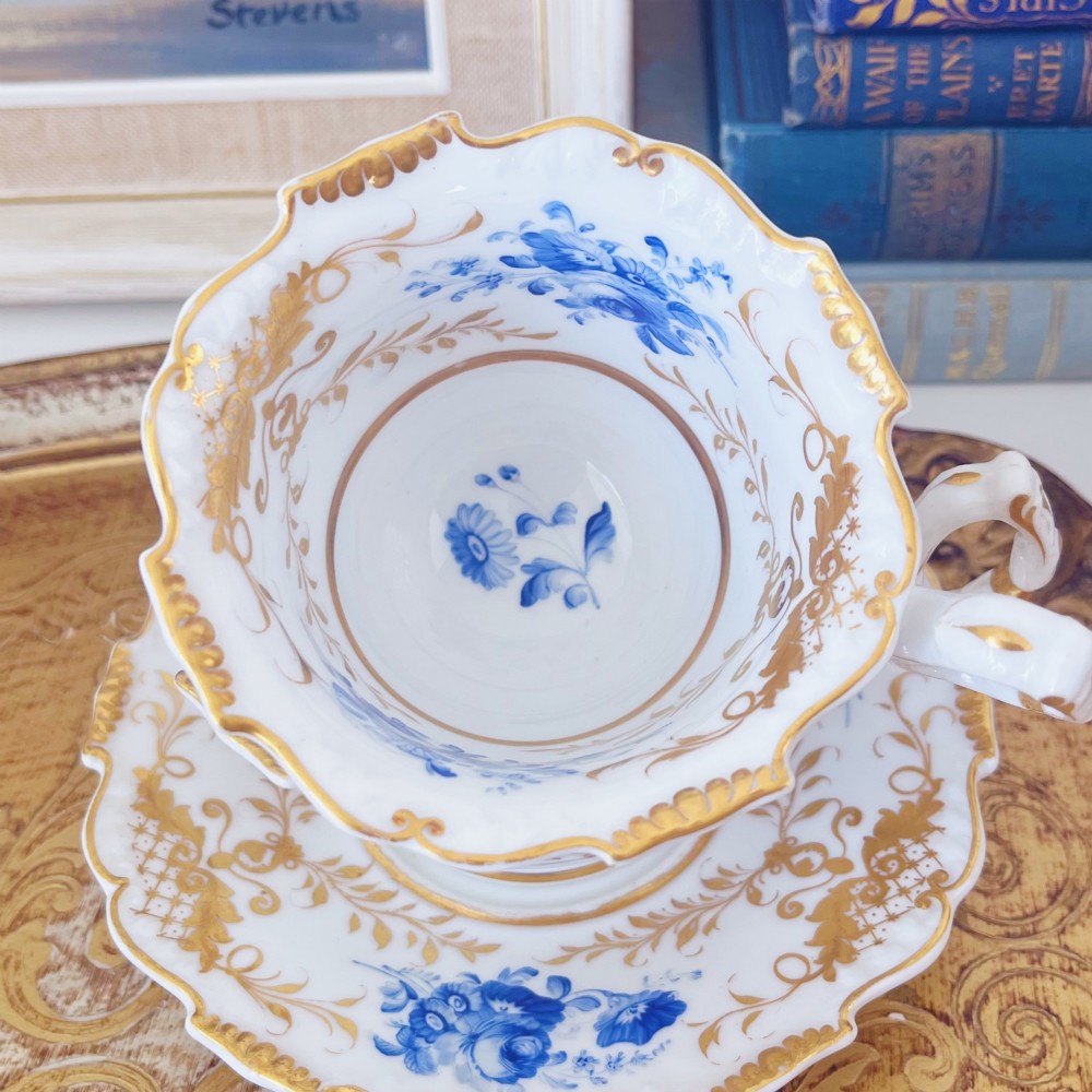 A Regency era porcelain tea trio comprising a teacup, coffee cup, and saucer decorated with blue floral hand-painting and gold leaf gilding. View III