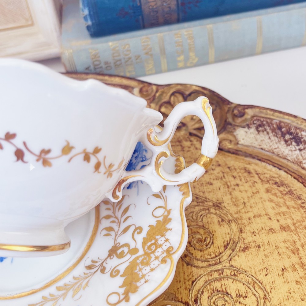 A Regency era porcelain tea trio comprising a teacup, coffee cup, and saucer decorated with blue floral hand-painting and gold leaf gilding. View VIII