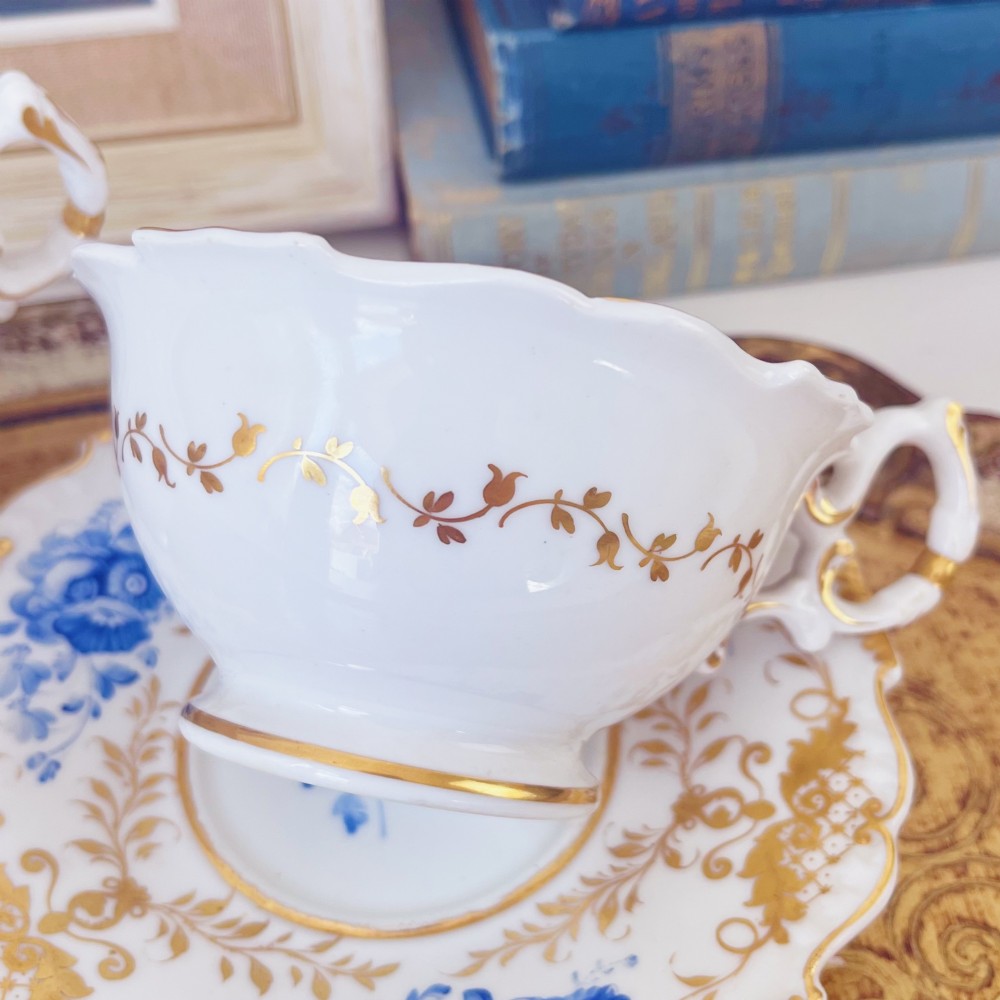 A Regency era porcelain tea trio comprising a teacup, coffee cup, and saucer decorated with blue floral hand-painting and gold leaf gilding. View IX