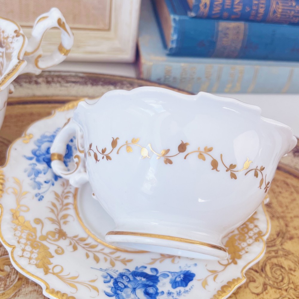 A Regency era porcelain tea trio comprising a teacup, coffee cup, and saucer decorated with blue floral hand-painting and gold leaf gilding. View X