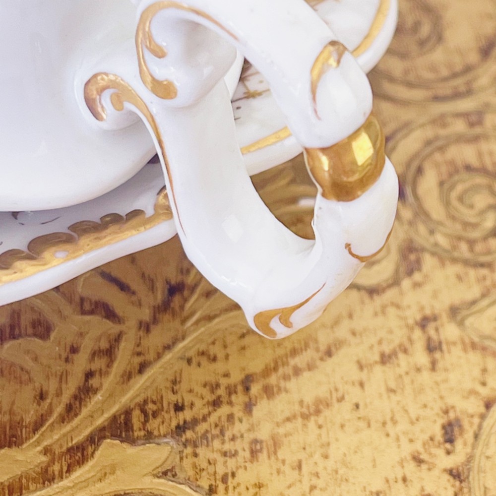 A Regency era porcelain tea trio comprising a teacup, coffee cup, and saucer decorated with blue floral hand-painting and gold leaf gilding. View XI