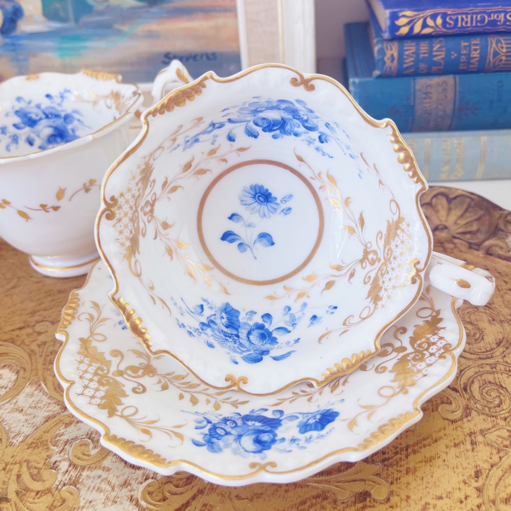 A Regency era porcelain tea trio comprising a teacup, coffee cup, and saucer decorated with blue floral hand-painting and gold leaf gilding. View XII