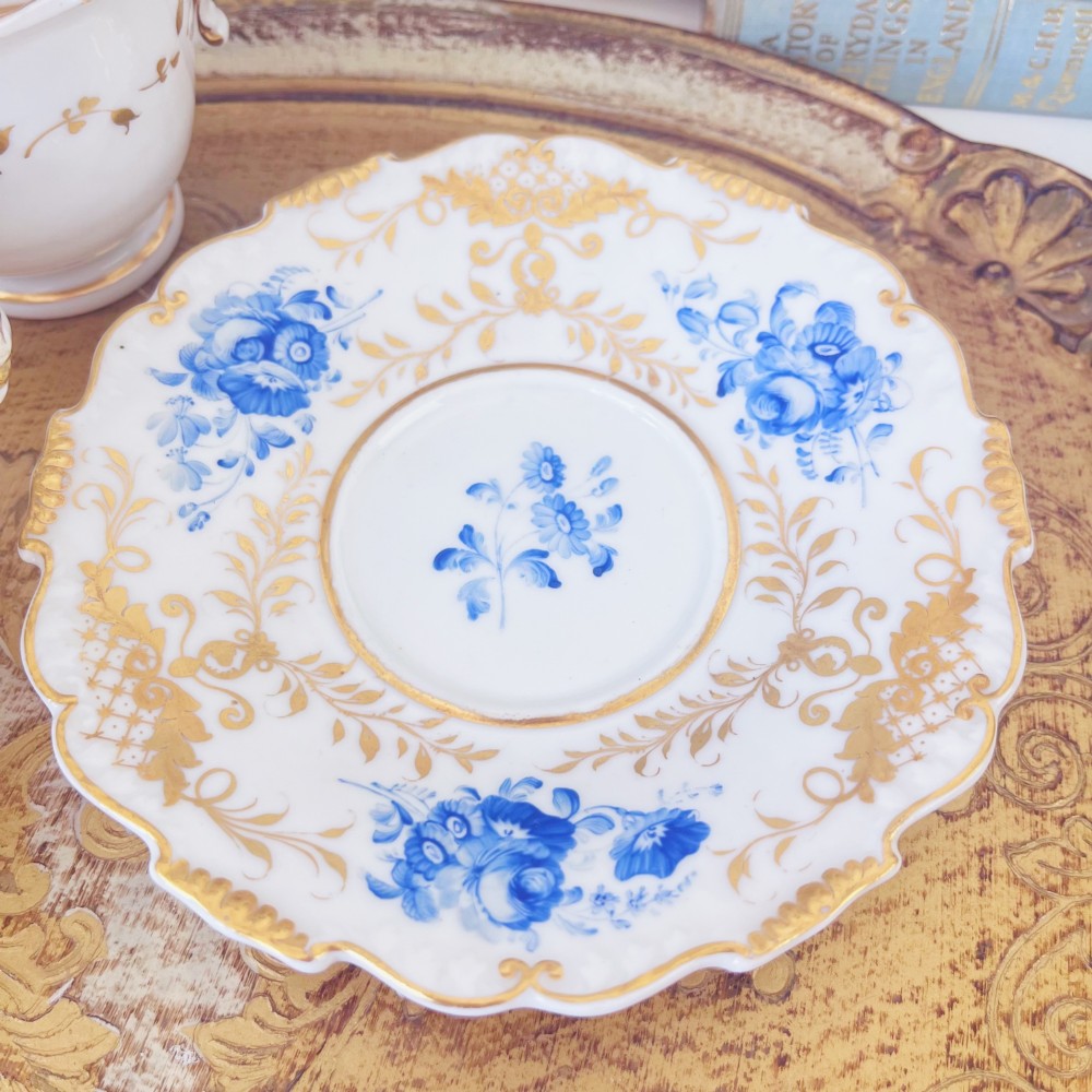 A Regency era porcelain tea trio comprising a teacup, coffee cup, and saucer decorated with blue floral hand-painting and gold leaf gilding. View XIII