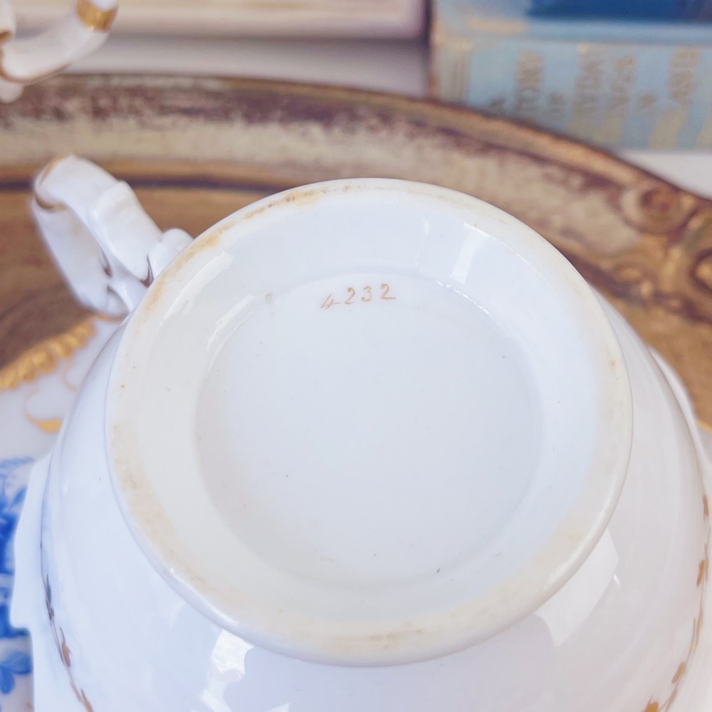 A Regency era porcelain tea trio comprising a teacup, coffee cup, and saucer decorated with blue floral hand-painting and gold leaf gilding. View XV